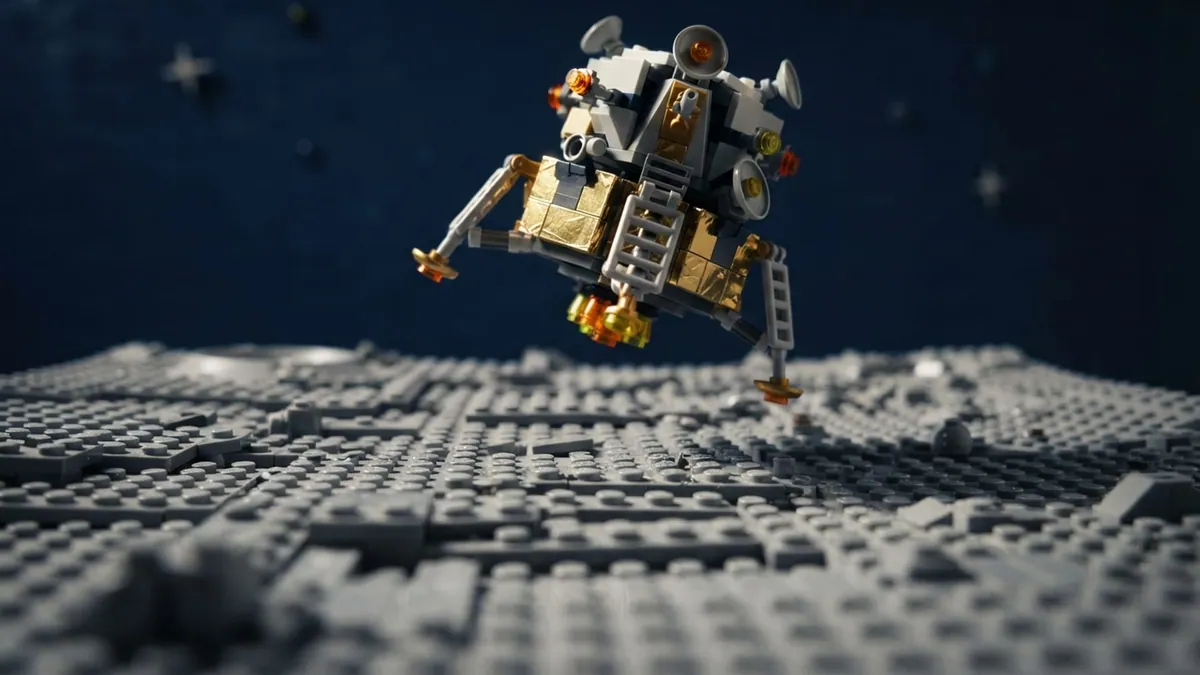 A toy-brick lunar lander hovering over a gray studded moon surface.