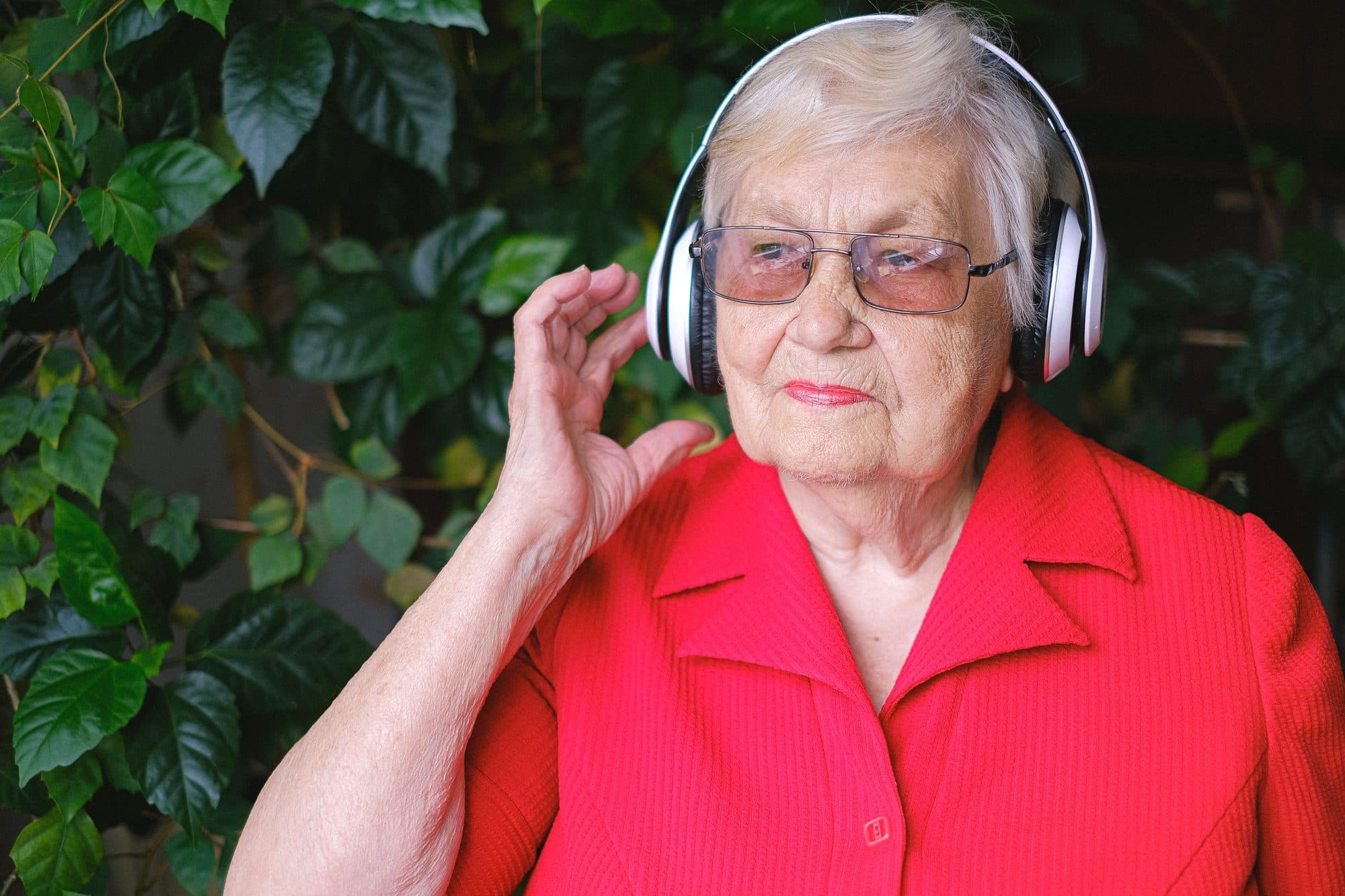 Elderly woman wearing headphones outdoors, listening to audio content