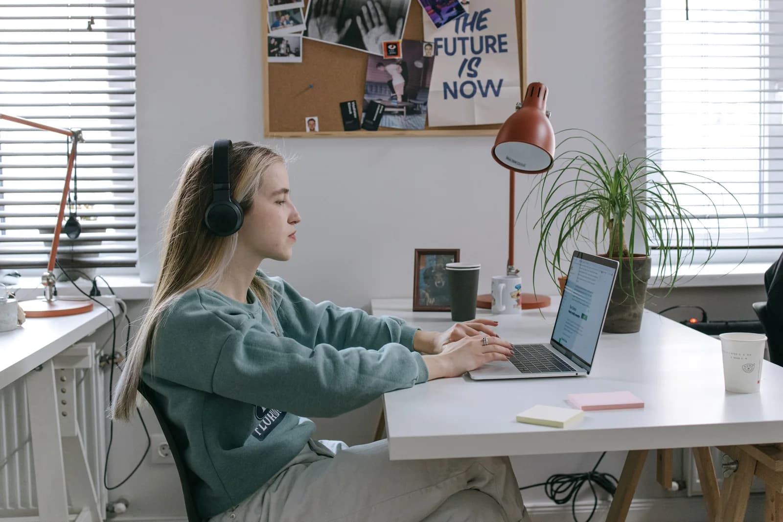 A woman wearing headphones and working on a laptop at her desk