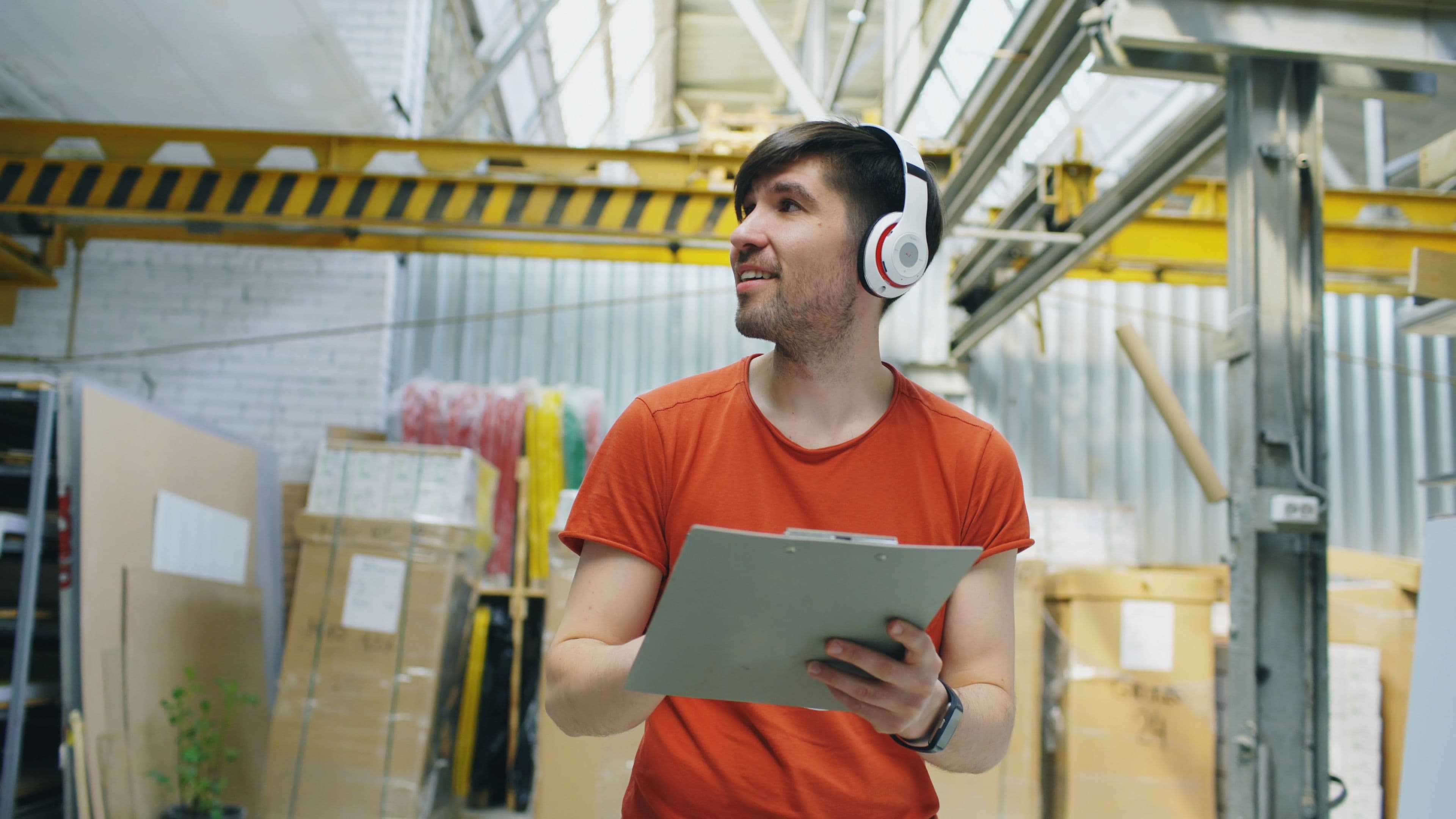Warehouse worker wearing headphones while checking inventory on a clipboard