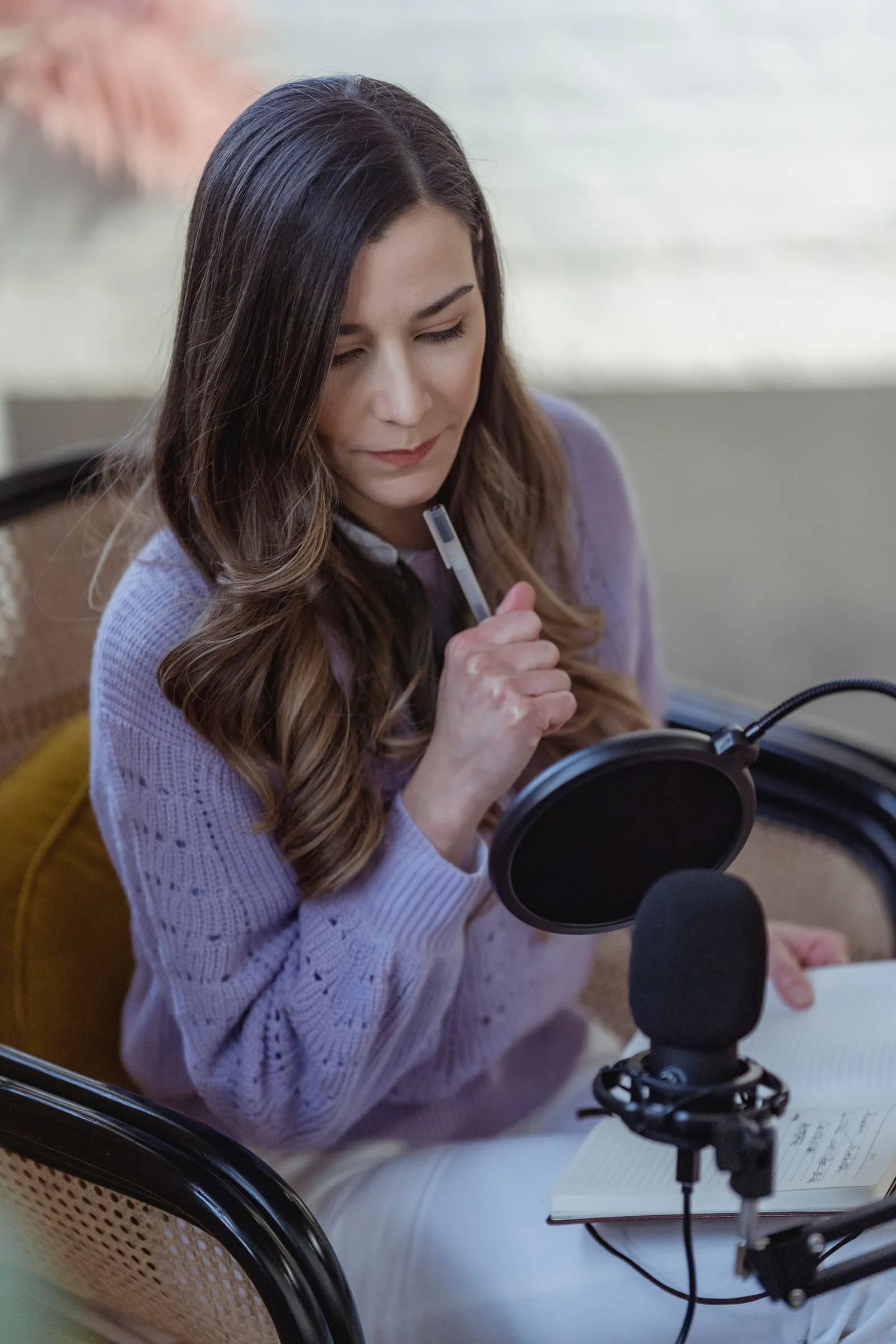 A woman with a notebook recording a podcast alone using a laptop and microphone