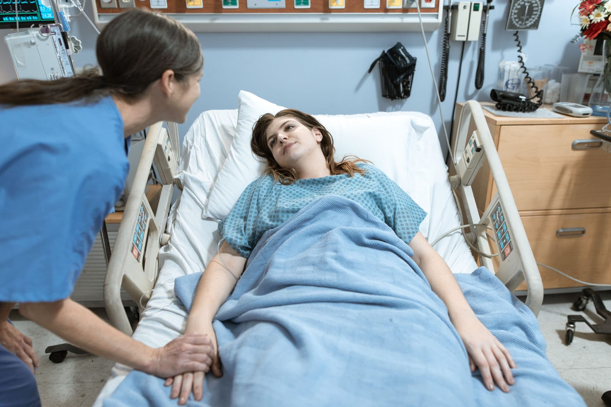 Nurse holding a patient's hand while talking with them in a hospital room
