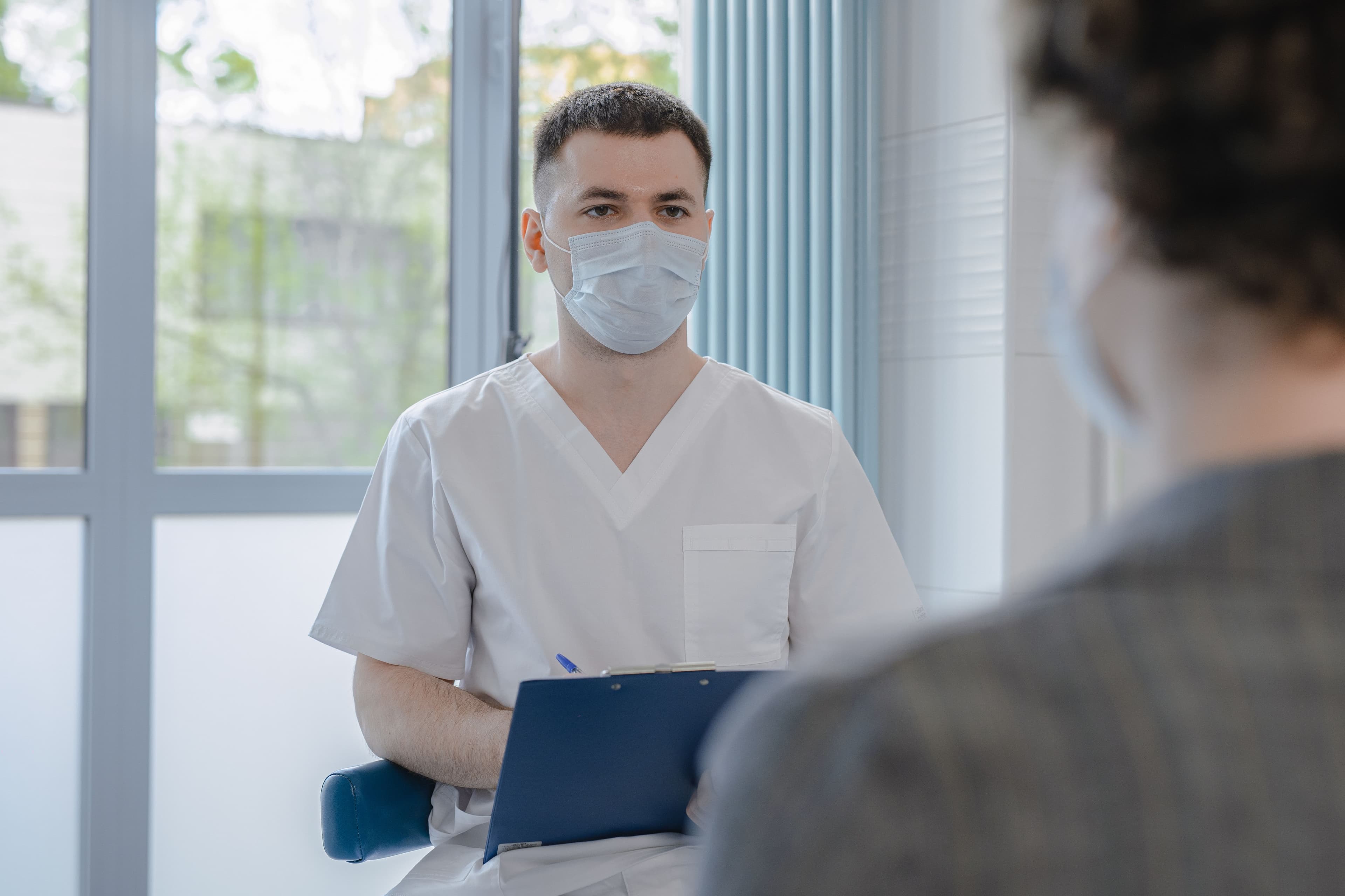 A clinician in scrubs talking with a patient while taking notes