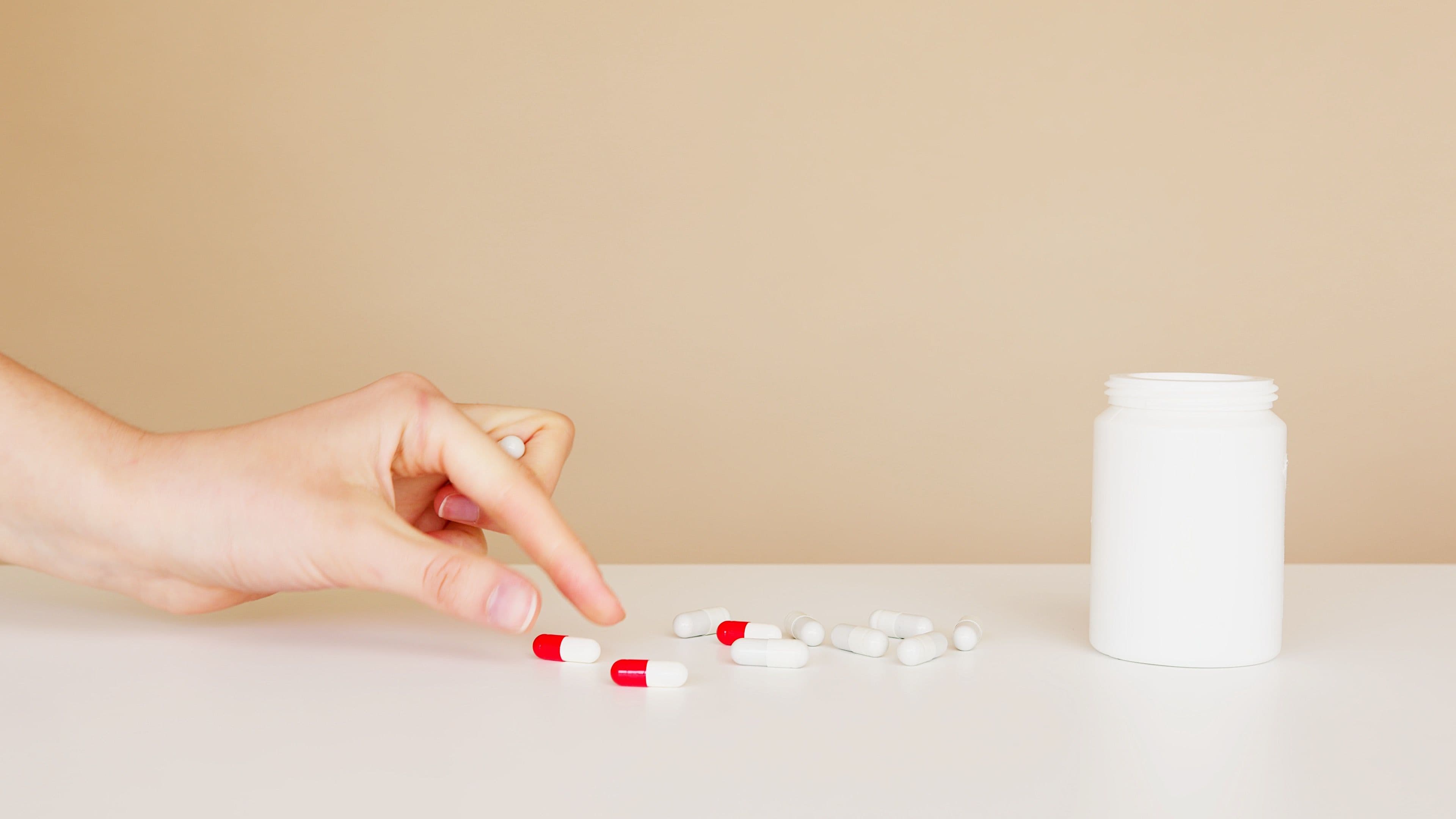 A hand reaching for a pill bottle on a table