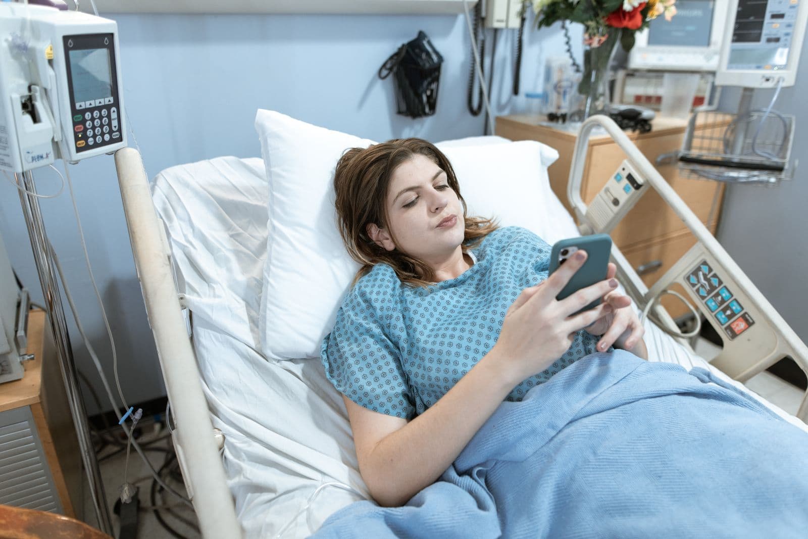 A patient lying in a hospital bed using a smartphone